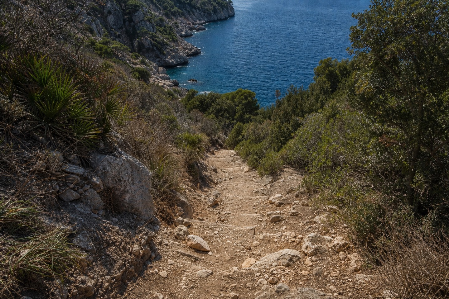 KI-generiertes Stimmungsbild eines steinigen, unebenen Abstiegswegs zu einer Bucht im Formentor-Stil