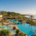 KI-generiertes Stimmungsbild einer familienfreundlichen Poollandschaft direkt am Sandstrand von Playa de Muro – keine Originalaufnahme des Grupotel Alcudia Pins.