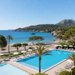 KI-Stimmungsbild für das Universal Hotel Castell Royal mit Außenpool, Kinderbecken, Palmen und direktem Übergang zum Strand von Canyamel