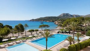 KI-Stimmungsbild für das Universal Hotel Castell Royal mit Außenpool, Kinderbecken, Palmen und direktem Übergang zum Strand von Canyamel