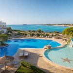KI-Stimmungsbild für das Universal Hotel Romántica mit Hauptpool, flachem Kinderpool, Wasserrutschen und Südmallorca-Küste